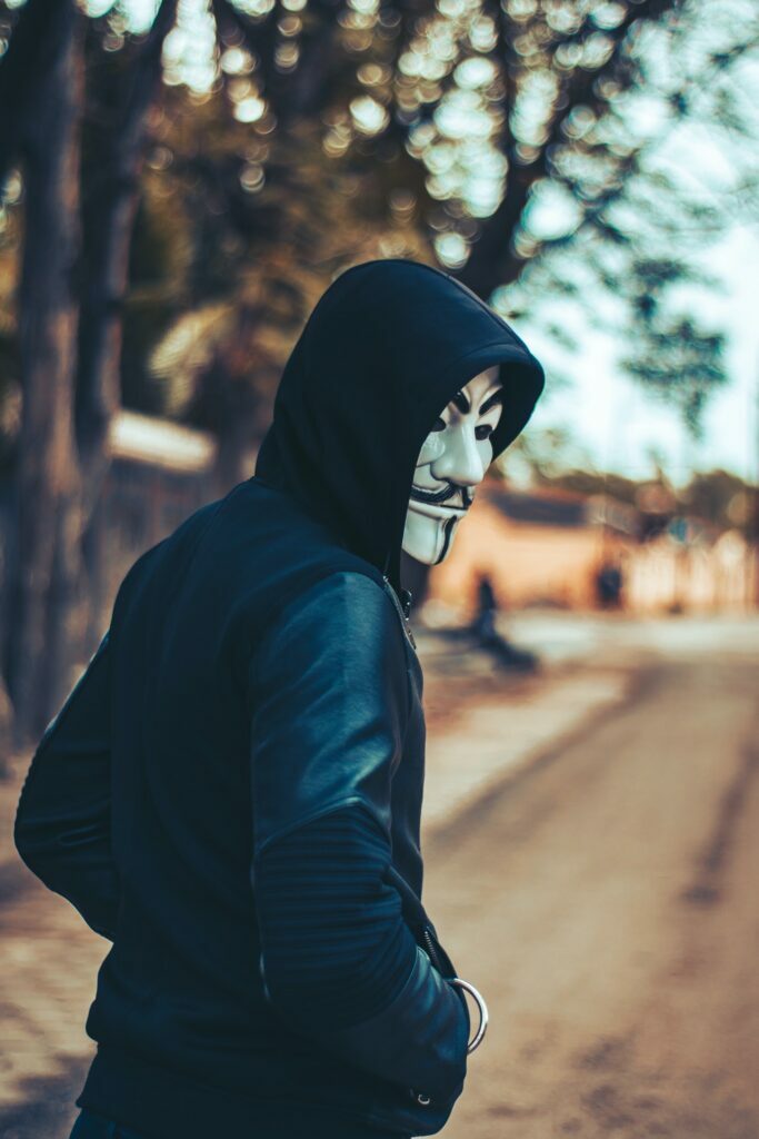 a hacker in an anonymous maks walking down a leafy street